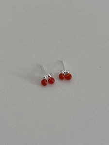 Macro shot of silver cherry earrings with red polished beads on a minimalist surface