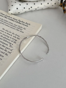 Detailed view of an irregular wavy silver bangle with a minimalist polished metal texture