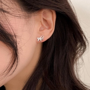 Close-up of minimalist S925 silver bow stud earrings worn by a model in a natural setting