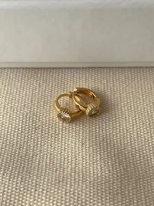 Macro shot of minimalist gold S925 silver hoop earring with sparkling zircon on fabric