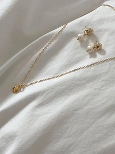 Détail d'un collier doré minimaliste avec pendentif ovale et boucles d'oreilles en perles