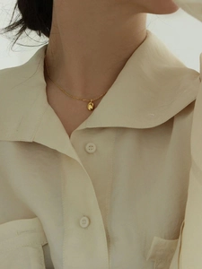 Collier minimaliste en argent 925 doré avec pendentif ovale sur un chemisier crème