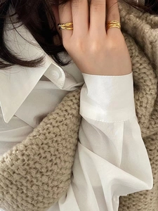 Detail of minimalist knotted gold rings paired with cozy beige autumn knitwear