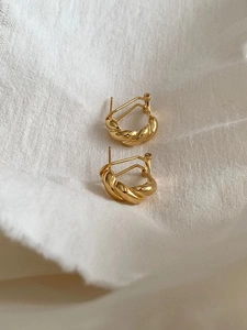 Macro view of gold twisted sterling silver hoop earrings on a white linen texture