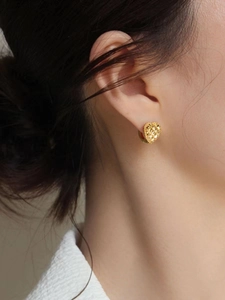 Detailed view of gold heart earrings with quilted texture worn by a model