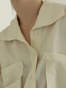 Collier avec pendentif ovale en argent 925 doré porté sur une chemise beige chic