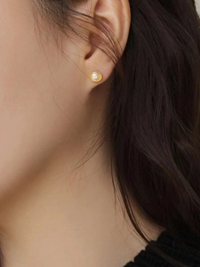 Close-up of elegant gold shell earring with a white freshwater pearl on the earlobe