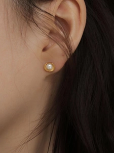 Detail of a shell-shaped gold stud earring with a round pearl worn on a model's ear