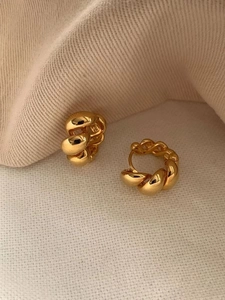 Detailaufnahme goldener gedrehter Creolen auf beige strukturiertem Stoff mit warmem Licht