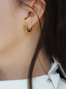 Close-up of gold square hoop earrings with textured vertical grooves worn by a model