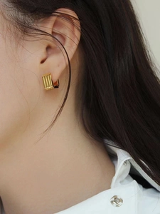 Close-up of golden square hoop earrings with vertical striped texture worn by a model