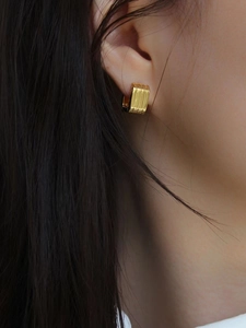 Detailed close-up of a small gold hoop earring with textured vertical stripe design