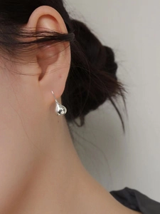 Close-up of minimalist silver water drop earrings worn on the earlobe