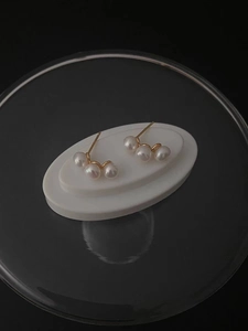 Close-up of three white pearls on a gold curved earring against a white pedestal