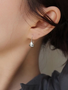 Macro view of mirror-polished silver teardrop earrings worn by a model in soft lighting