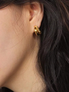Macro view of gold double twisted rope C-shaped earrings worn by a female model