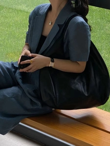 Close-up of black leather tote bag with natural texture shown on a female model outdoors