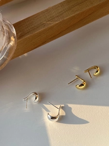 Detailed view of silver and gold C-shaped minimalist stud earrings in natural sunlight