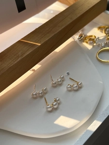 Detailed view of three-pearl curved stud earrings in gold plating on a display tray