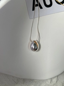 Close-up of a silver-toned teardrop pendant with a fine snake chain on a white tray