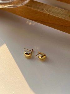 Detailed view of glossy 18K gold bean-shaped minimalist stud earrings in a warm setup
