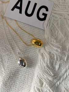 Macro shot of gold and silver double-sided water drop necklaces on white knit background