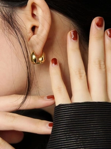Close-up of high-polish gold oval hoop earrings showing the mirror finish and minimalist design