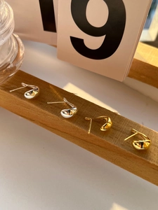 Polished silver and gold bean-shaped stud earrings displayed on natural wood stand