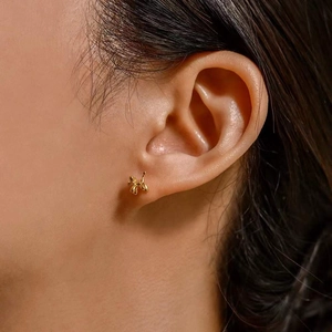 Close-up of polished gold balloon dog stud earring worn on ear with high metallic luster