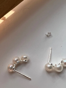 Macro shot of 925 sterling silver curved earrings with three white pearls on white box