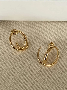 Détail de boucles d'oreilles créoles torsadées dorées sur un fond en lin beige naturel