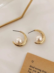 Detailed close-up of C-shaped gold hoop earrings with white pearls on marble surface