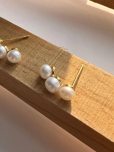 Macro shot of 925 silver gold-plated pearl earrings with three pearls on a wood block