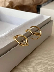 Détail de créoles torsadées en métal doré posées sur le bord d'une boîte à bijoux blanche