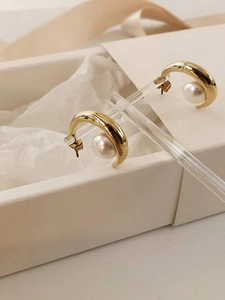 Elegant C-shaped gold-plated silver earrings featuring round white pearls on a display