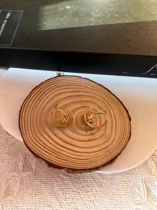 Vue de dessus de boucles d'oreilles dorées croisées sur un support minimaliste en bois