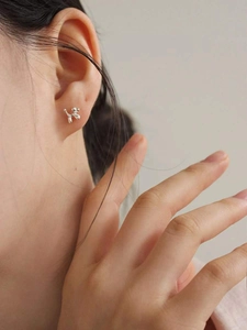Close-up of a glossy silver balloon dog stud earring worn by a model in a minimalist style