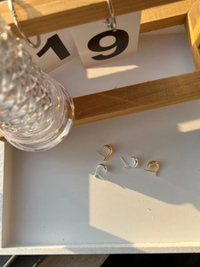 Close-up of minimalist gold and silver C-shaped hoop earrings on a decorative white tray