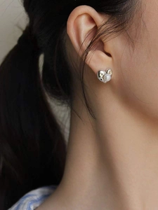 Detailed view of a silver heart-shaped earring with a pearl on a model's ear