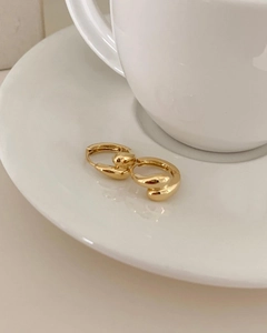 Close-up of polished gold teardrop earrings placed on a minimalist white ceramic tray