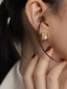 Close-up of a 925 silver heart earring with textured gold finish and a white pearl