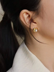 Close-up of golden heart earrings with white pearls worn on ear for elegant style