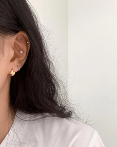 Detailed view of layered 925 silver stud earrings, pearl hoops, and gold ear cuffs on ear