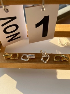 Minimalist geometric gold and silver U-shaped chain earrings on a wooden stand