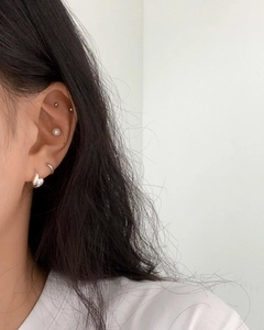 Close-up of multiple 925 silver stud earrings and hoops worn on earlobes and cartilage
