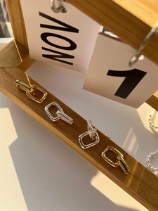 Detail view of gold and silver U-shaped 925 silver earrings hanging on wood decor