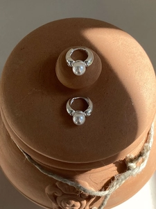 Elegant silver pearl hoop earrings presented on a vintage ceramic texture background