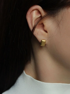 Detail of matte gold rectangular stud earrings on a model with a minimalist aesthetic