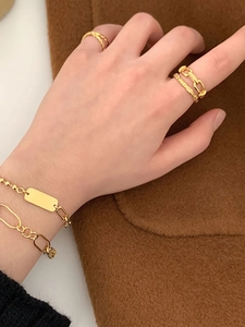 Dettaglio di anelli e bracciali in argento S925 dorato su tessuto marrone di tendenza