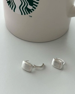 Detailed close-up of rectangular brushed silver stud earrings on a minimalist background